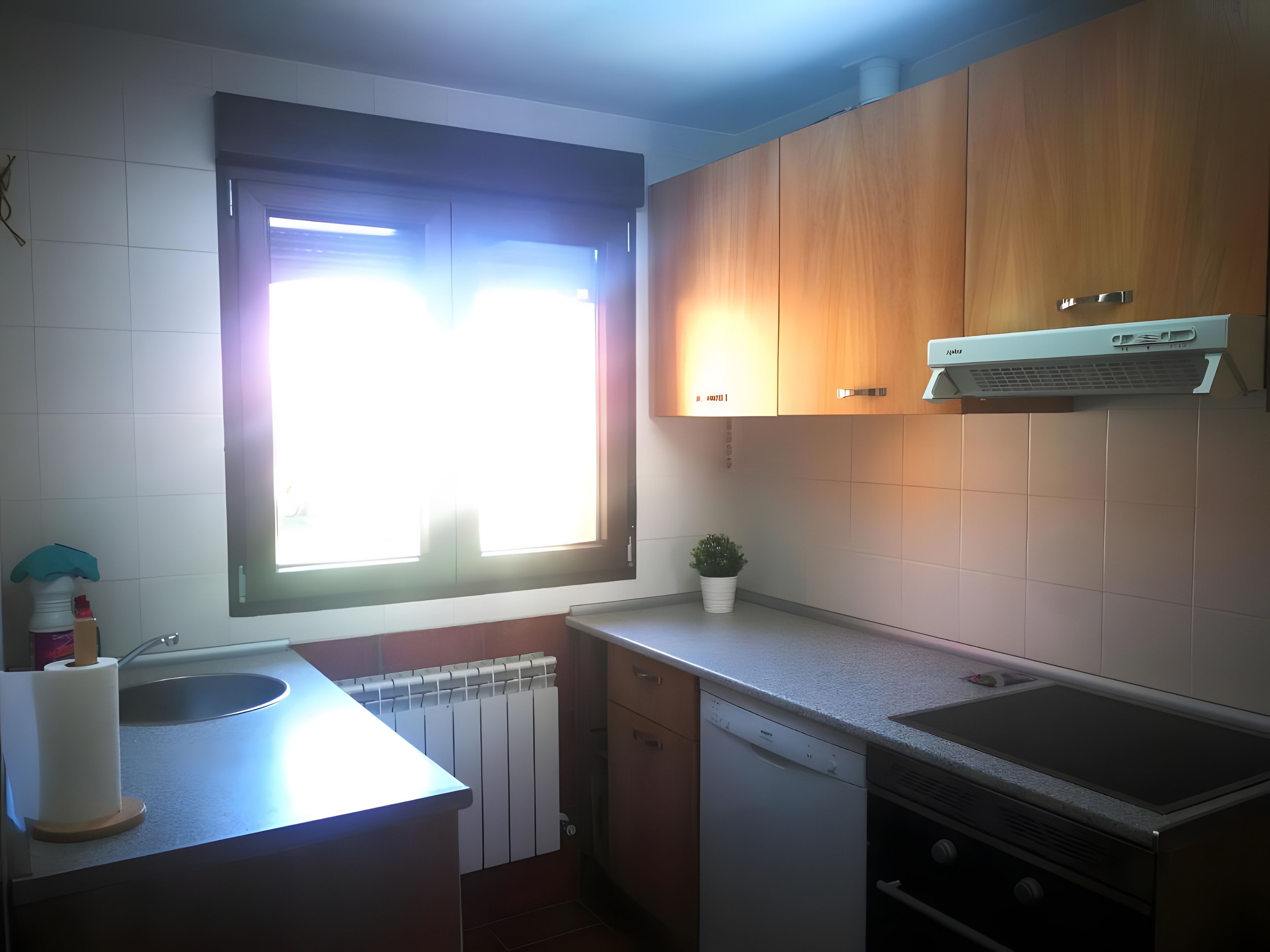 Una cocina con ventana, radiador, lavavajillas y armarios de madera.