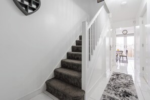 Eine Treppe mit Teppichstufen führt zu einem hellen Flur mit weißen Wänden und einem gemusterten Teppich.
