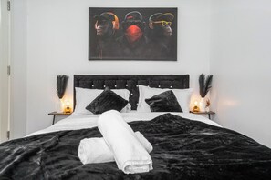 A bedroom with a black headboard, white bedding, and a painting above the bed. - Stylish 5-Bed for 12 w/ Pool & Table Tennis Near Etihad & Co-op Live (Droylsden)