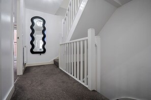 Un corridoio con ringhiera bianca, pavimento rivestito di tappeto e specchio con cornice nera.