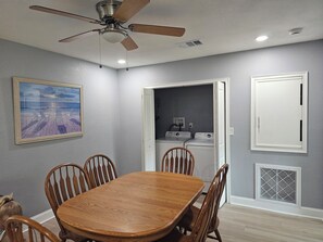 A dining area with a wooden table and chairs, a ceiling fan, a painting on the wall, and a laundry room with washing machines. - Lovely 2-bedroom house with AC in charming Englewood with Boat slip to Lemon Bay (Englewood)