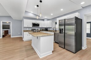 A modern kitchen with white cabinetry, stainless steel appliances, and a granite countertop island. - Lovely 2-bedroom house with AC in charming Englewood with Boat slip to Lemon Bay (Englewood)