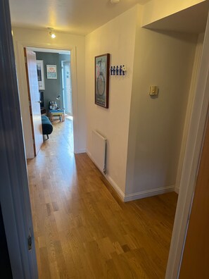 A hallway with wooden flooring, a radiator, and a door leading to another room. - One Double Room in Holyrood Apartment (Edinburgh)