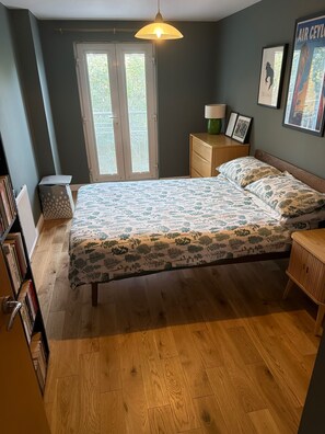 A bedroom with a bed, a nightstand, a lamp, a window with blinds, and a bookshelf. - One Double Room in Holyrood Apartment (Edinburgh)
