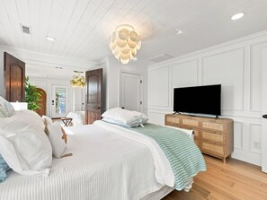 Een slaapkamer met een groot bed, een televisie op een houten dressoir en een plafondlamp.