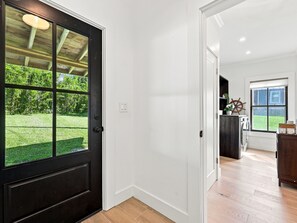A hallway with a black door leading to a room with a view of a green lawn. - Historic Swansboro Retreat | Water Views + Backyard with Pizza Oven (Swansboro)