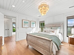 A bedroom with a wooden bed, a large window, and a ceiling light fixture. - Historic Swansboro Retreat | Water Views + Backyard with Pizza Oven (Swansboro)