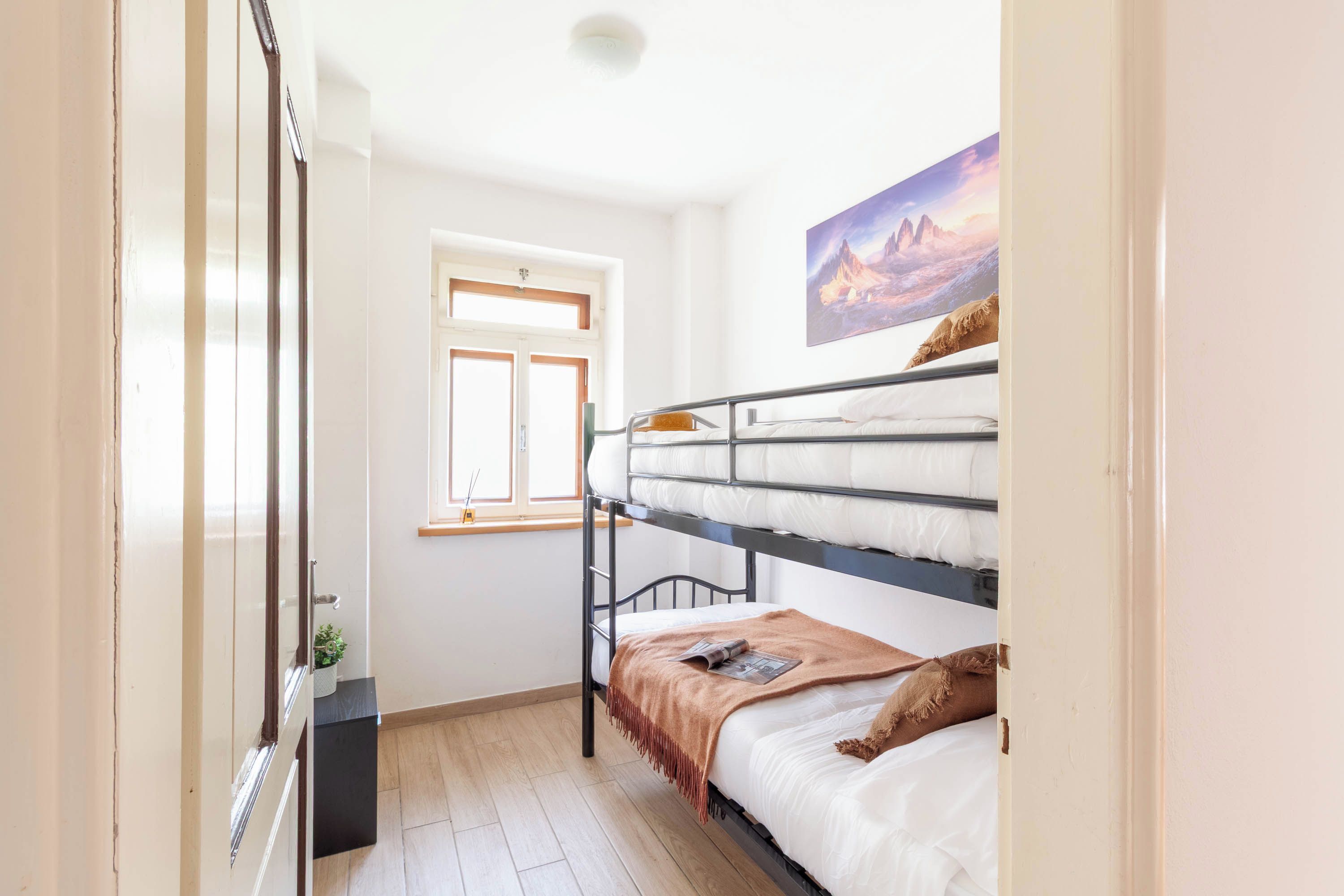 A dormitory room with bunk beds, a window, and a painting on the wall.
