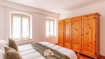 Une chambre à coucher avec un lit, une armoire en bois et deux fenêtres avec des rideaux.