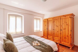 Un dormitorio con una cama, un armario de madera y dos ventanas con cortinas.