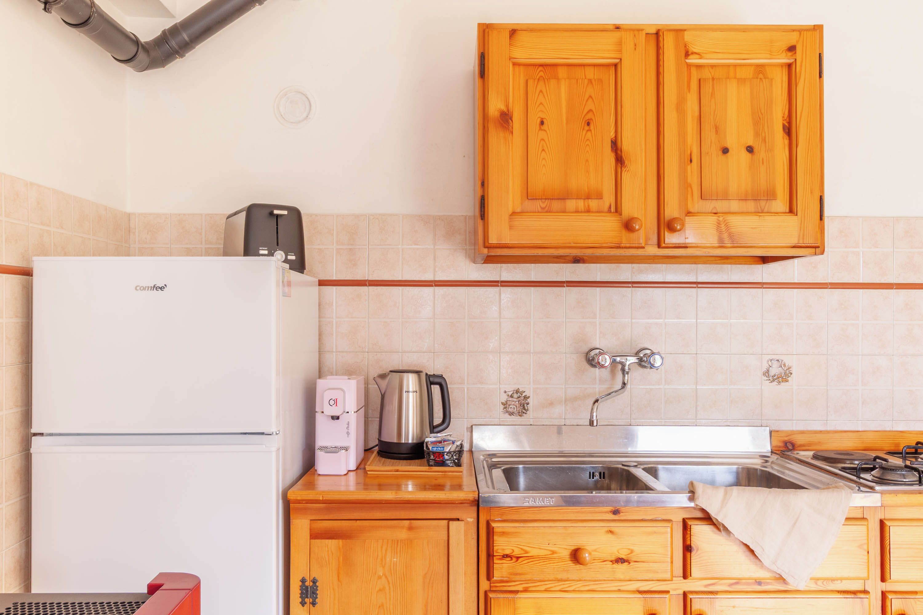 Une cuisine avec des meubles en bois, un réfrigérateur blanc, une machine à café, une bouilloire et un évier.