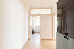 Un couloir au plancher de bois mène à une pièce où se trouve un meuble de couleur sombre.