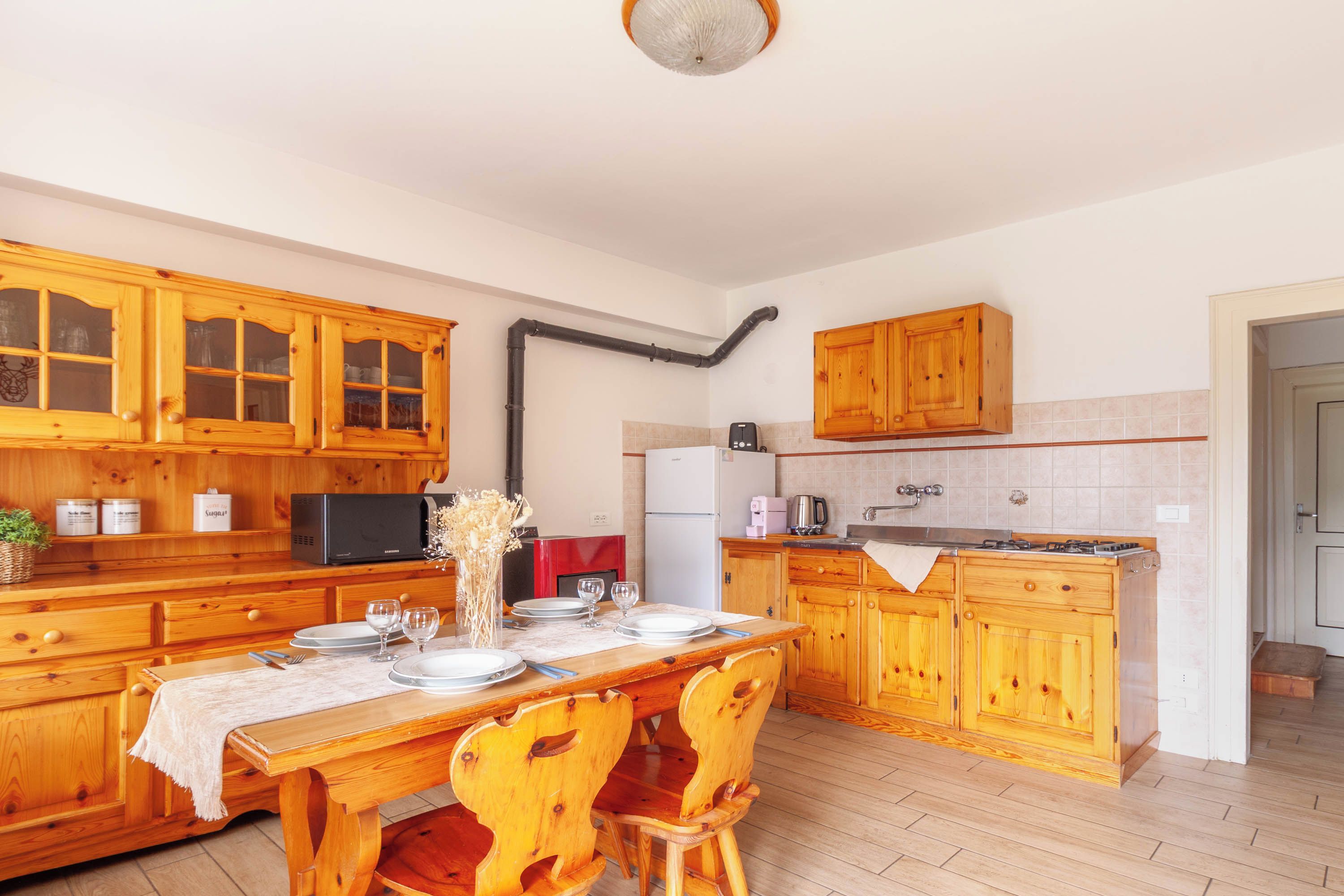 Une cuisine avec des meubles de rangement en bois, une table à manger dressée pour quatre personnes et un tuyau noir apparent au plafond.