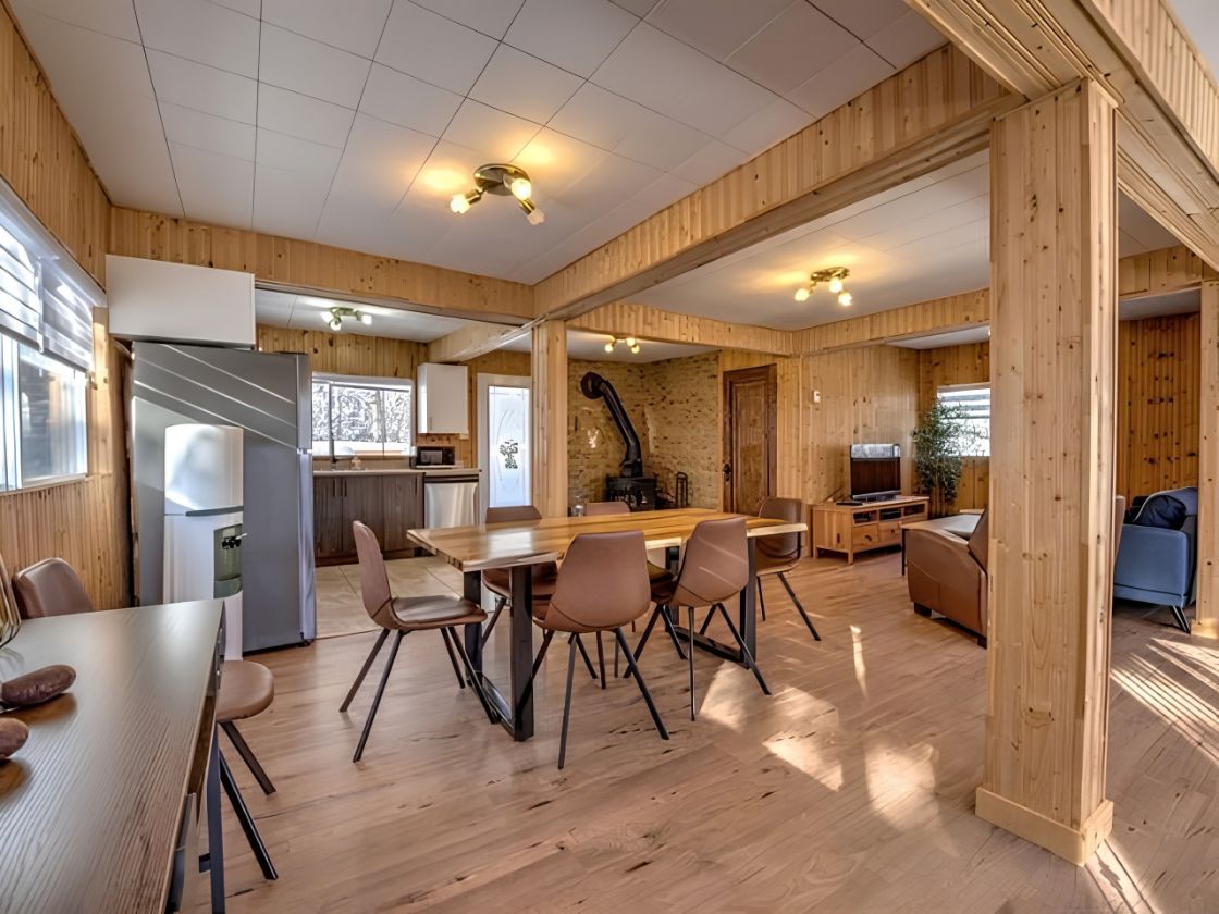 Ett modernt kök med träpanel på väggarna, en matplats med stolar och en tv.