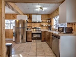 A modern kitchen with stainless steel appliances, wooden cabinetry, and a tiled floor.