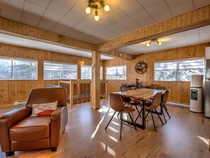 A wooden-paneled room with a dining table and chairs, a leather chair, and a refrigerator. - Vrbo Property (Nominingue)
