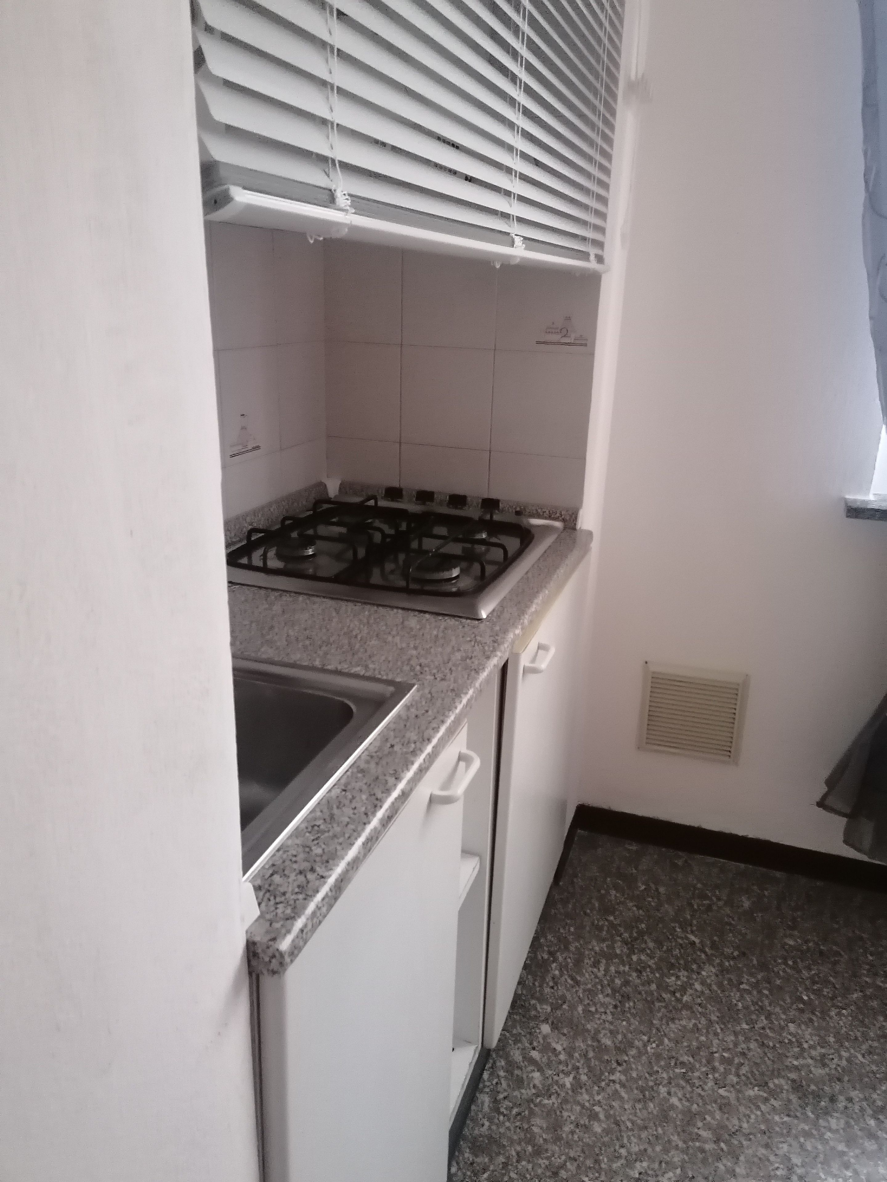 Une cuisine équipée d’une cuisinière à gaz, de meubles blancs et d’une fenêtre avec des stores.