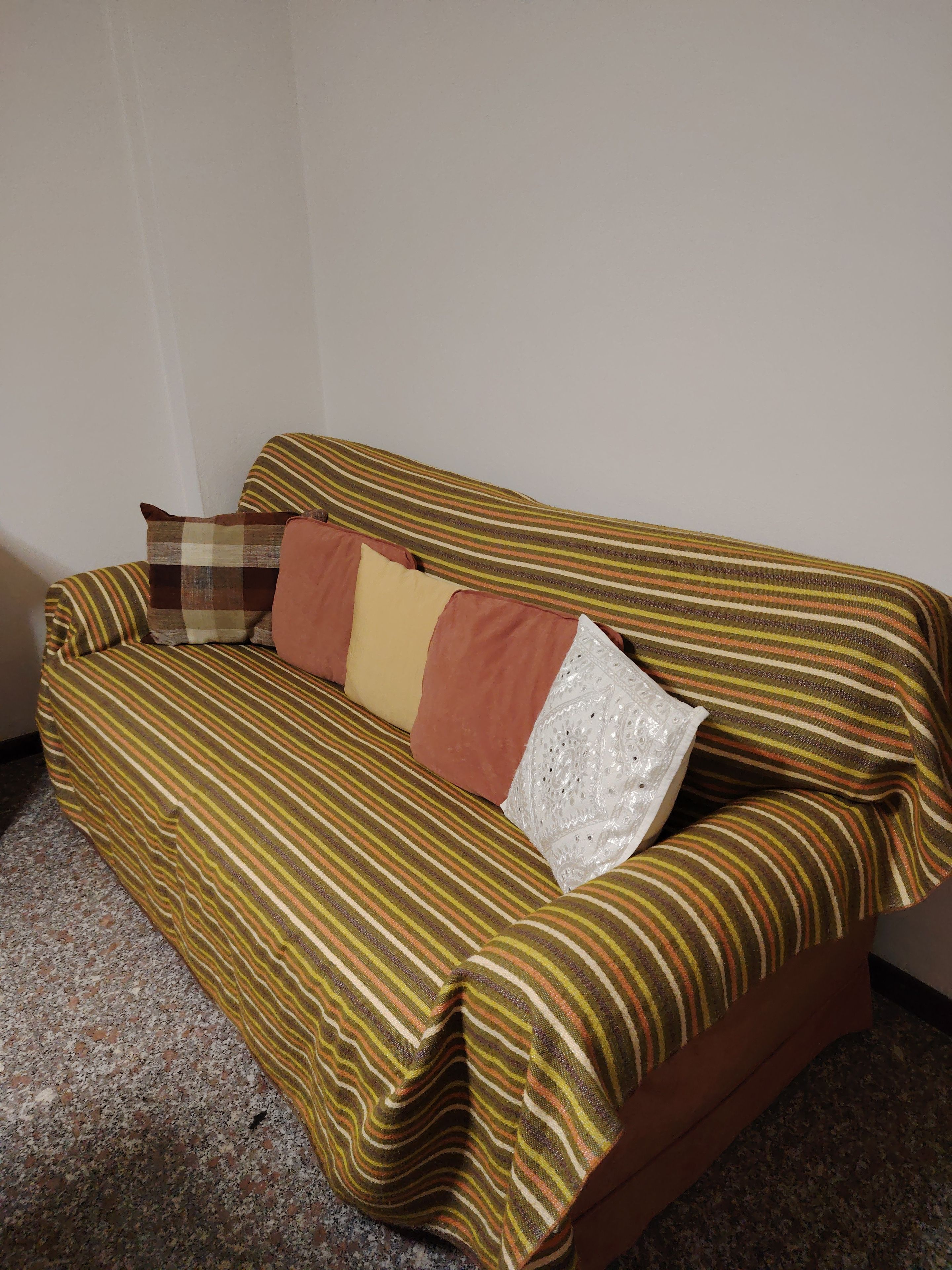 Ein Sofa mit gestreifter Auflage und mehreren Kissen in einem Raum mit schlichter Wand und punktiertem Boden.