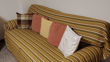 Ein Sofa mit gestreifter Auflage und mehreren Kissen in einem Raum mit schlichter Wand und punktiertem Boden.