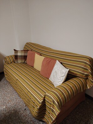 Un canapé recouvert d’un tissu à rayures, agrémenté de plusieurs coussins, dans une pièce dont le mur est uni et le sol parsemé de motifs.