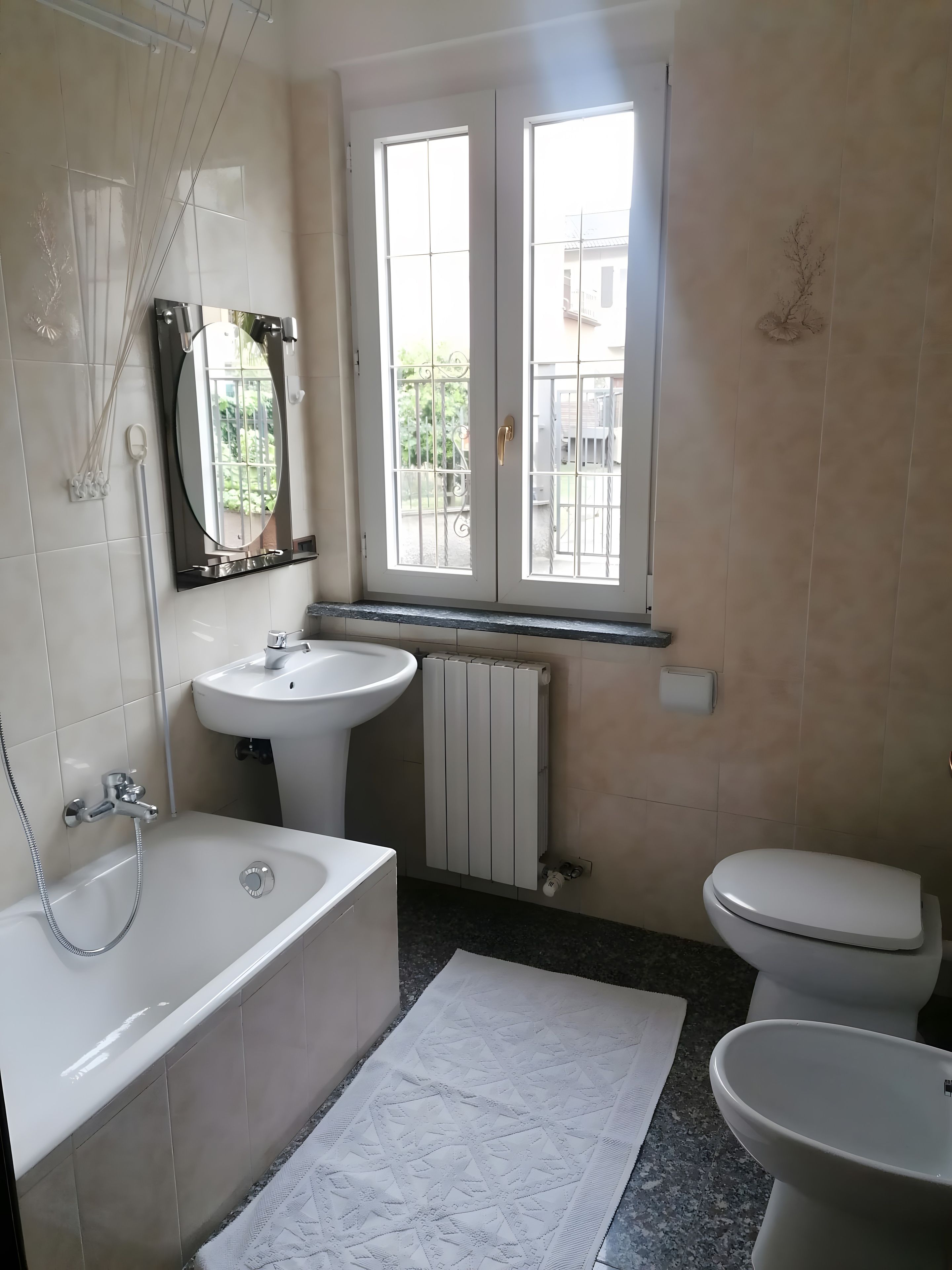 Ein Badezimmer mit Badewanne, Waschbecken und Toilette. Ein Fenster bietet einen Blick nach draußen.