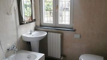 Ein Badezimmer mit Badewanne, Waschbecken und Toilette. Ein Fenster bietet einen Blick nach draußen.