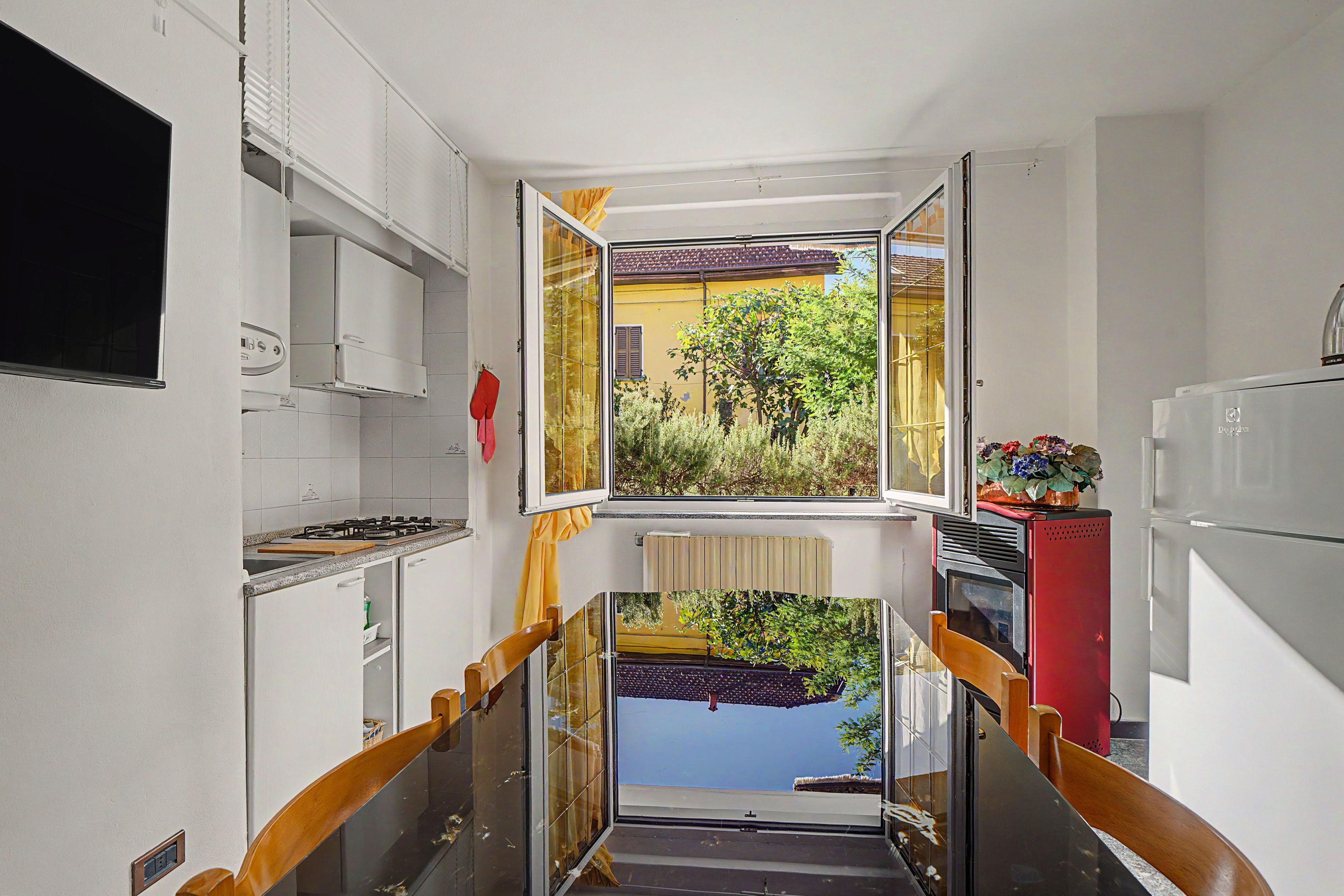 Une cuisine étroite donnant sur un jardin, avec un réfrigérateur rouge et une cuisinière.
