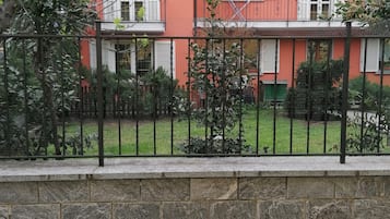 Ein zweistöckiges Gebäude mit einer Steinmauer im Vordergrund und einem Metallzaun.