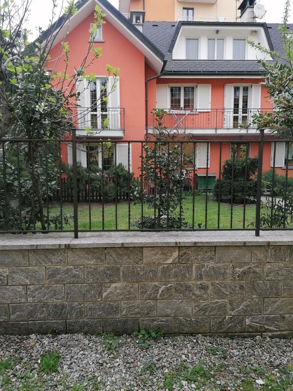 Ein zweistöckiges Gebäude mit einer Steinmauer im Vordergrund und einem Metallzaun.
