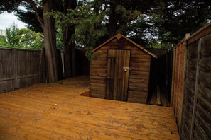 A wooden shed with a door and a small opening, surrounded by a wooden fence and trees. - Central Wembley - Apartment - Sleeps 5 - Parking (Wembley)