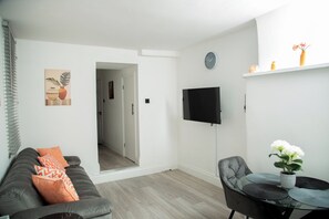 A modern living room with a sofa, a dining table with chairs, a flat-screen TV, and a potted plant. - Central Wembley - Apartment - Sleeps 5 - Parking (Wembley)