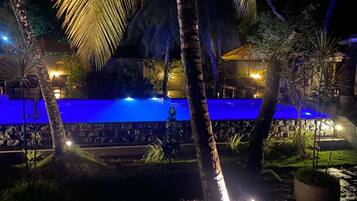Vue nocturne d’un espace piscine éclairé de lumières bleues, entouré de palmiers et d’un mur de pierre.