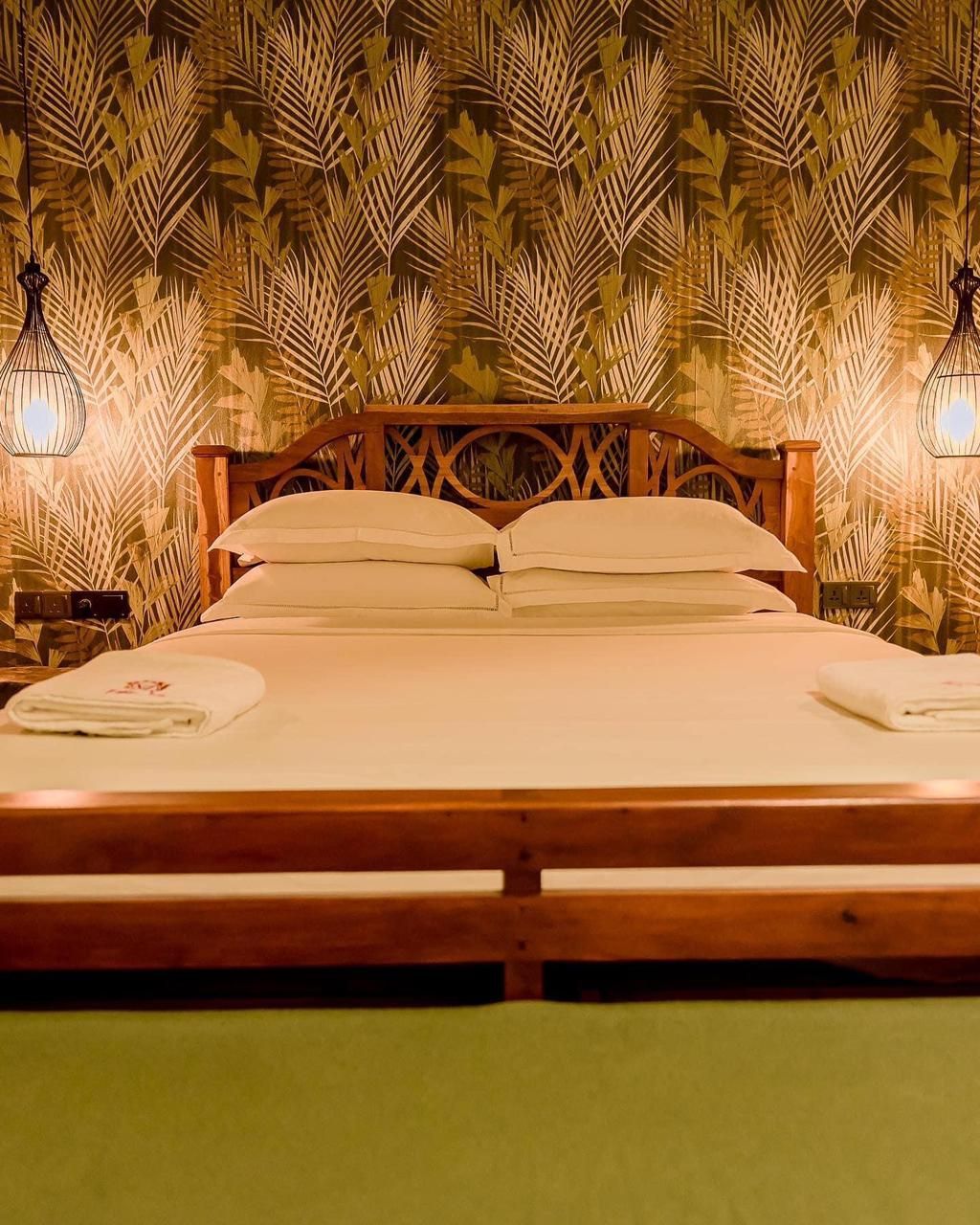 Un lit avec une tête de lit en bois, deux lampes de chevet et un papier peint à motifs.