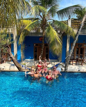 A group of people in a swimming pool with palm trees and a blue building in the background. - RELAX AND UNWIND AT LU XURY MODERN VILLA DC (Talpe)