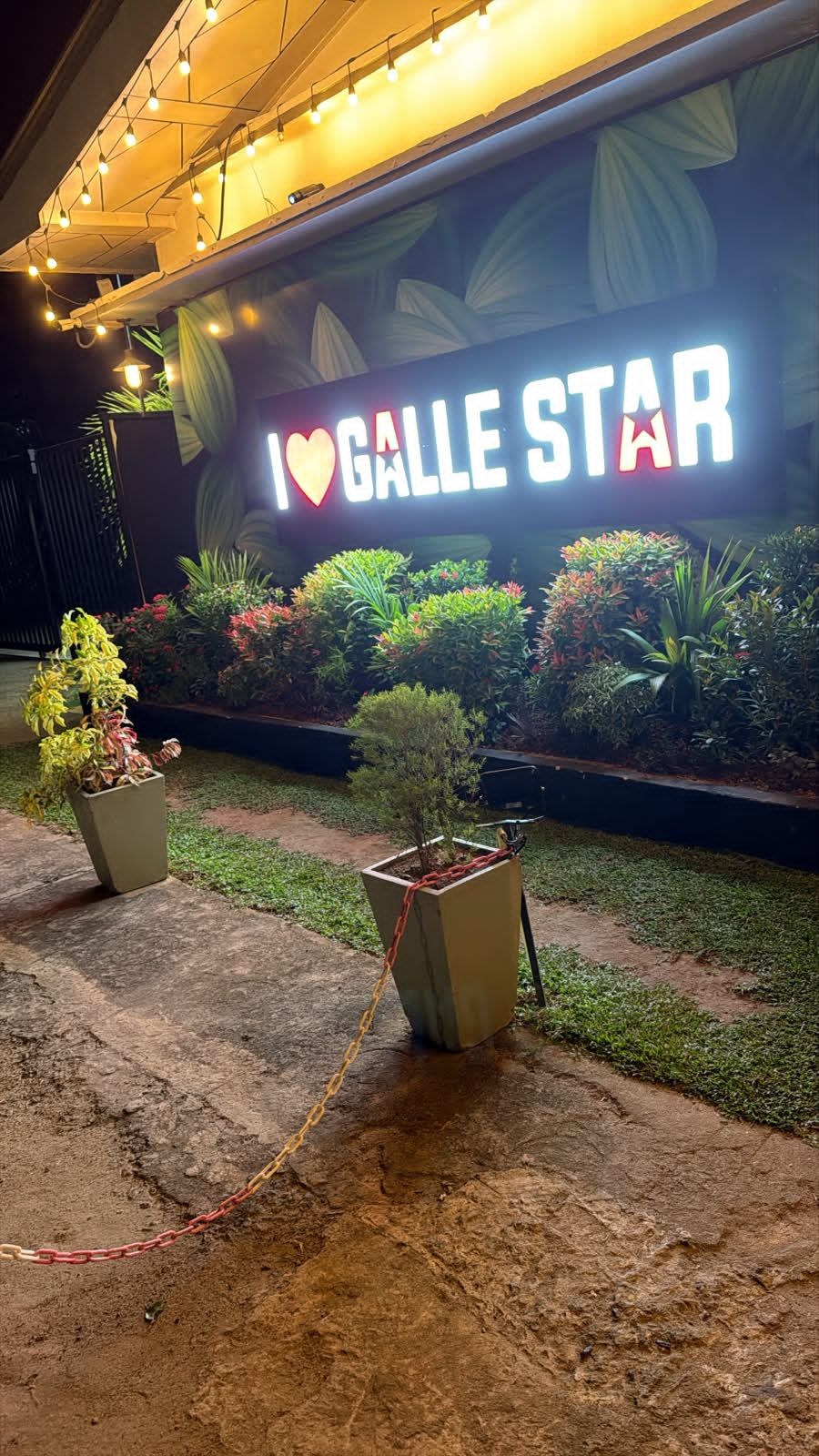 Ein Schild mit der Aufschrift 'I ♥ GALLLE STAR', umgeben von Blumentöpfen und einem Betonweg.