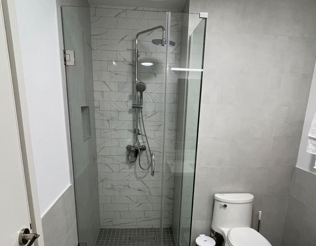 Casa de banho moderna com cabine de duche de vidro, sanita e parede com efeito mármore.