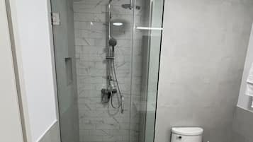 Casa de banho moderna com cabine de duche de vidro, sanita e parede com efeito mármore.