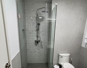 A modern bathroom with a glass-enclosed shower, a toilet, and a marble-patterned wall. - Sol Harbour Apartment in Ocho Rios (Ocho Rios)