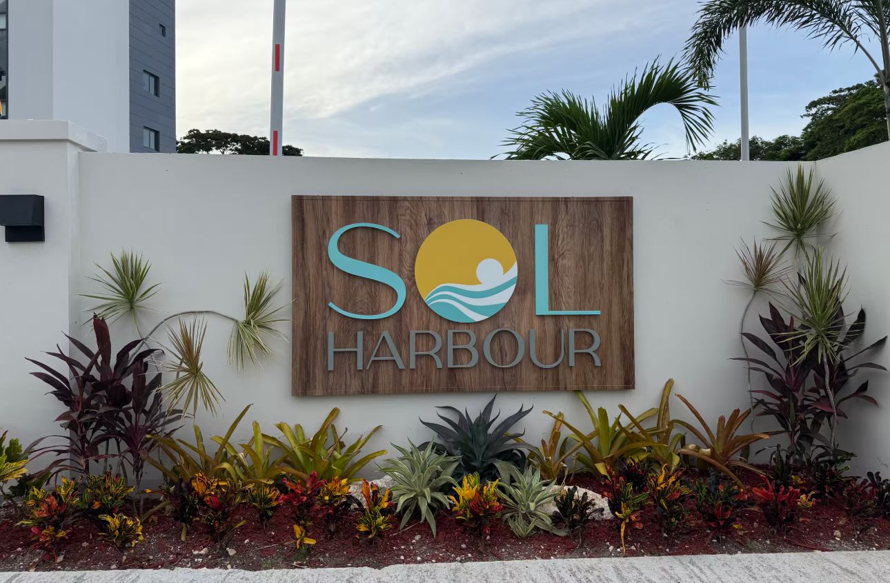 A sign for 'SOL HARBOUR' with a logo featuring a sun and wave, surrounded by various tropical plants.