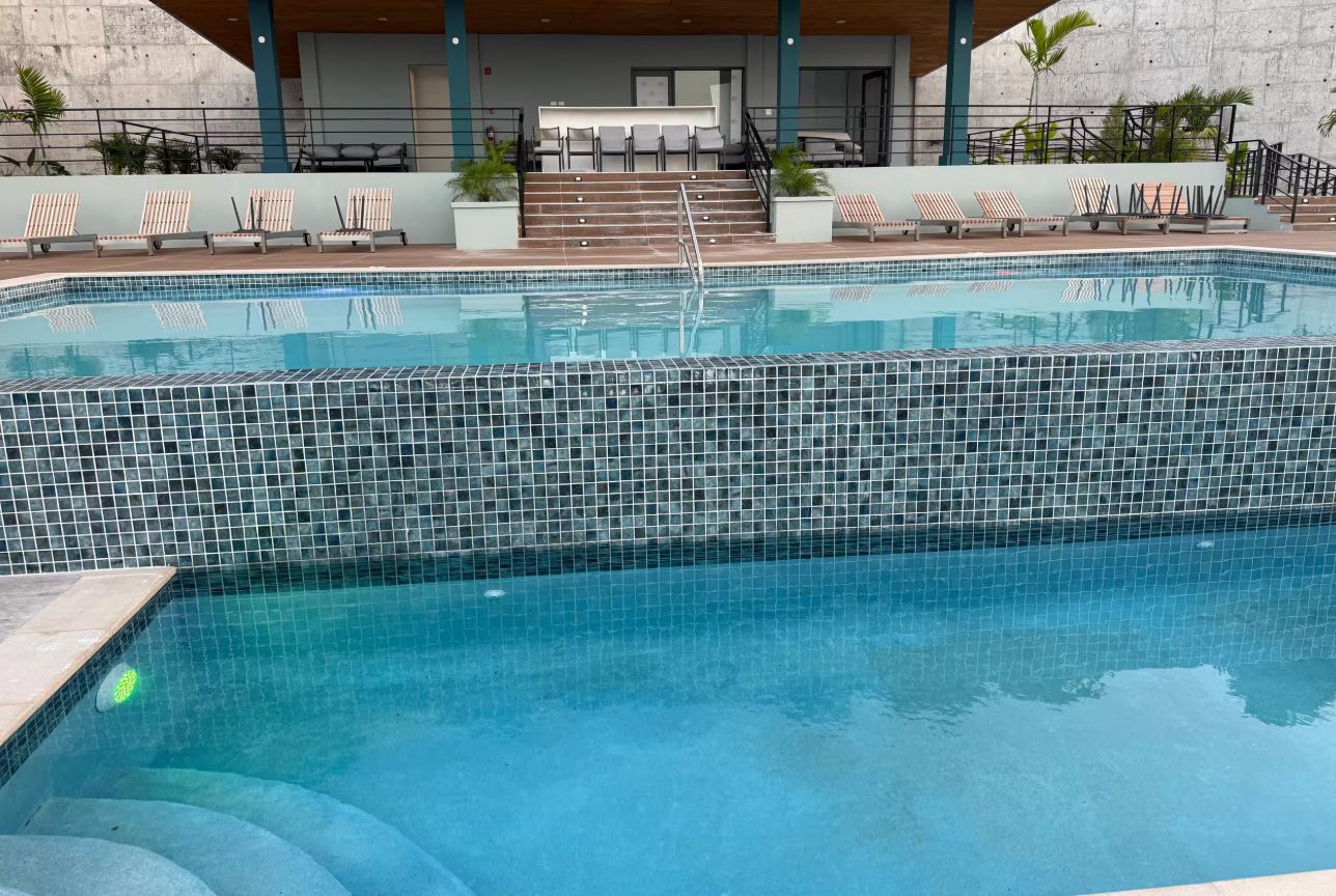 A swimming pool with tiled edges, a covered seating area with chairs, and a staircase leading to an upper level.