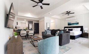 A modern living room with a sofa, armchair, and coffee table. There is a dining area with chairs and a table. The room has a ceiling fan and an air conditioning unit. - Sol Harbour Apartment in Ocho Rios (Ocho Rios)