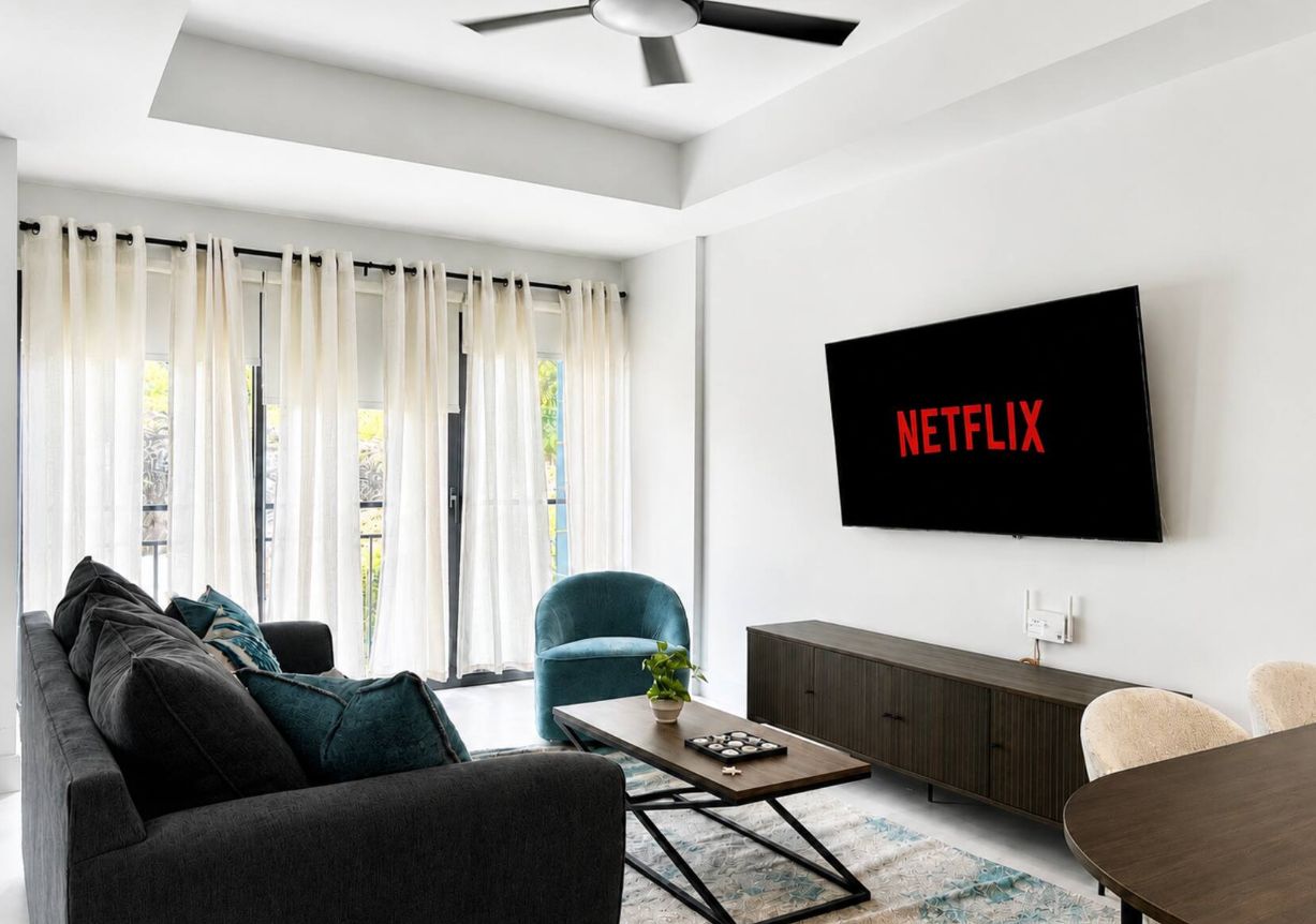 A modern living room with a sofa, a coffee table, a blue armchair, and a television mounted on the wall displaying the Netflix logo.
