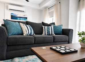A modern living room with a dark grey sofa, patterned cushions, a wooden coffee table with decorative items, and a potted plant. - Sol Harbour Apartment in Ocho Rios (Ocho Rios)