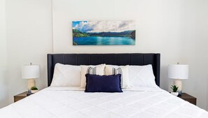 A neatly made bed with a white quilt, a dark headboard, and two bedside lamps. - Sol Harbour Apartment in Ocho Rios (Ocho Rios)