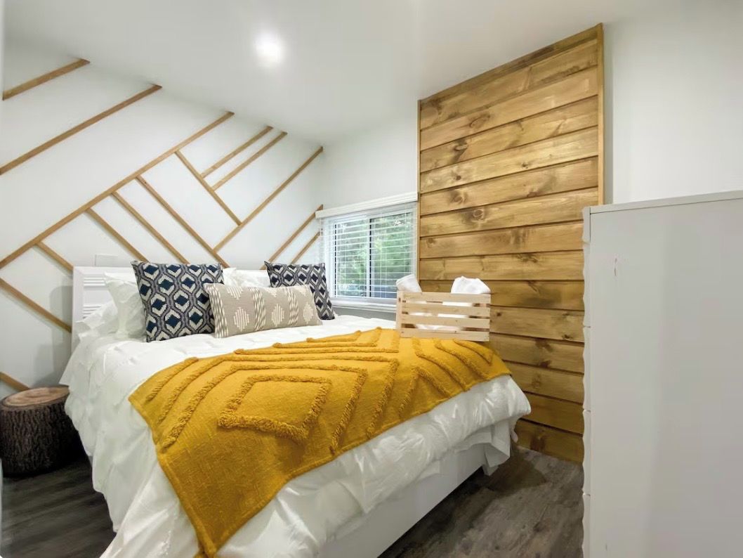 A bedroom with a bed, wooden wall paneling, a window with blinds, and a white wardrobe.