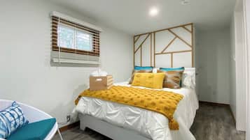 A bedroom with a bed, a chair, a window with blinds, and a wall with a geometric pattern.