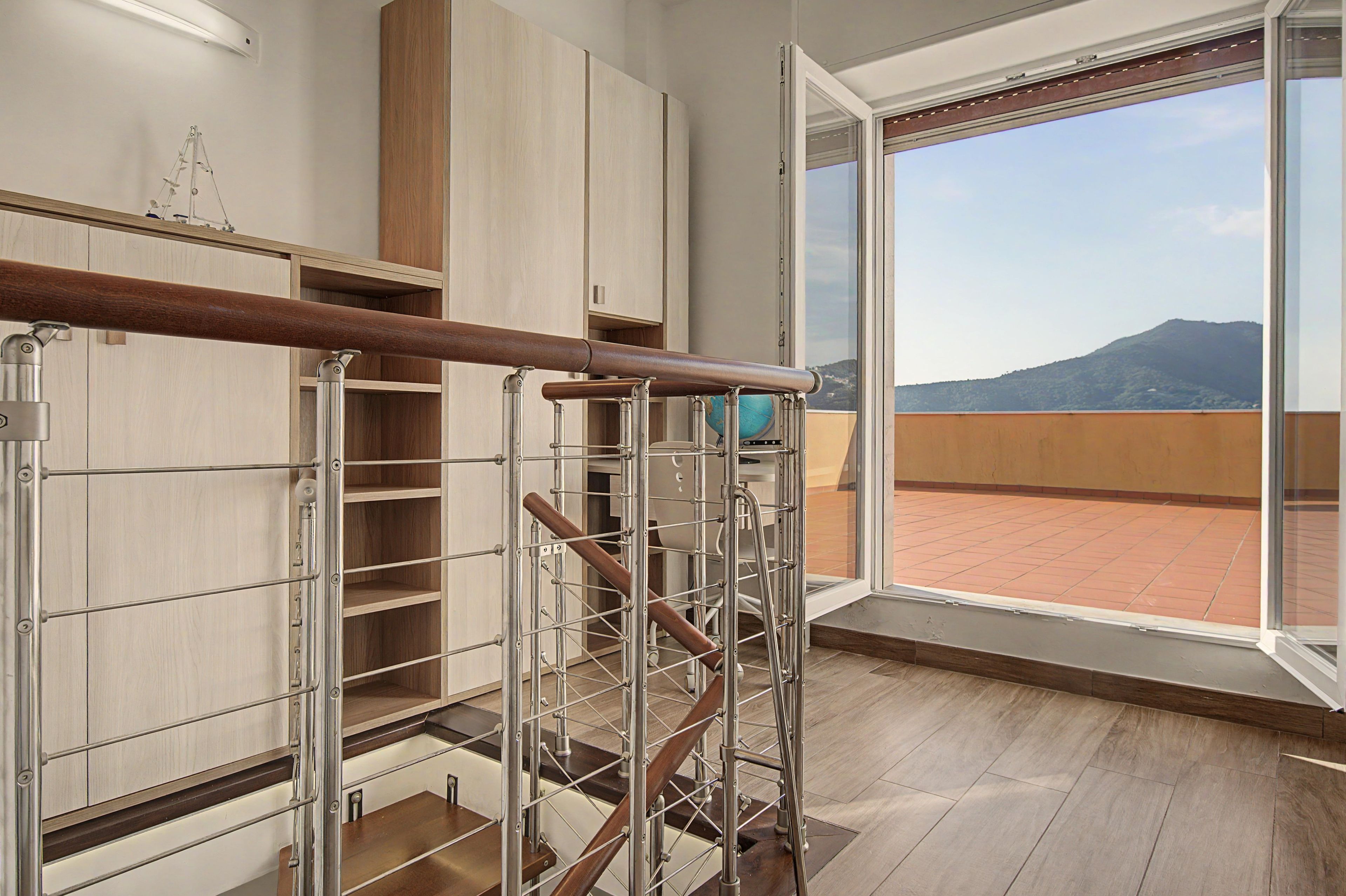 Ein modernes Interieur mit einer Holztreppe, Metallgeländern und einem großen Fenster mit Blick auf eine gebirgige Landschaft.