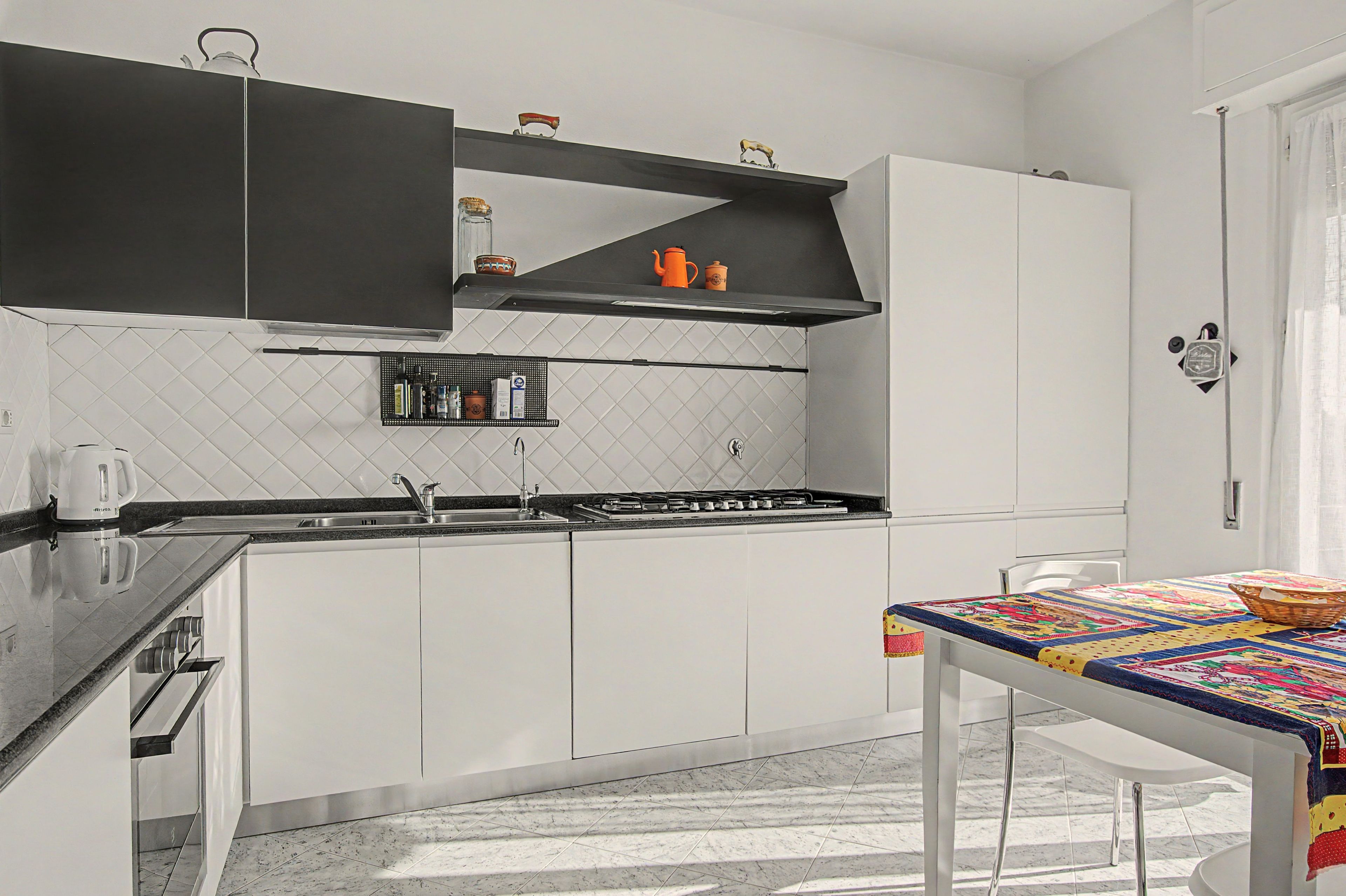 Cocina moderna con armarios blancos, encimera negra y pileta de acero inoxidable.