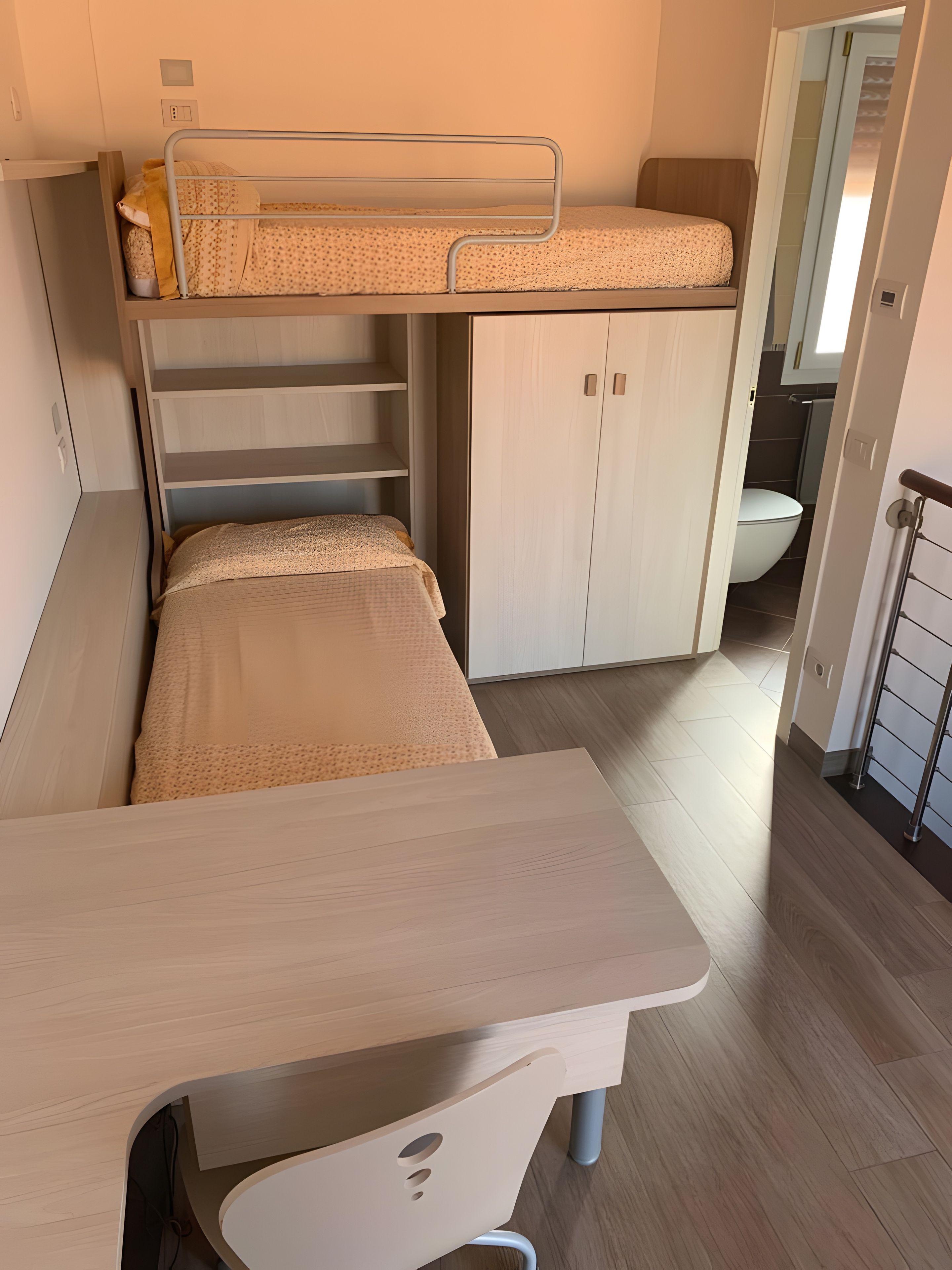 Un lit superposé avec un bureau en dessous, une armoire et une salle de bain à l’arrière-plan.