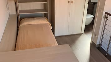 Un lit superposé avec un bureau en dessous, une armoire et une salle de bain à l’arrière-plan.
